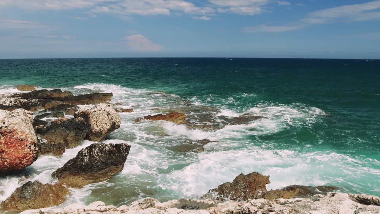 雄伟的舞蹈:一瞥从岩石悬崖绿松石海洋体验强大的海浪的绿松石海洋撞击崎岖的岩石从一个惊人的观点在悬崖上。视频素材