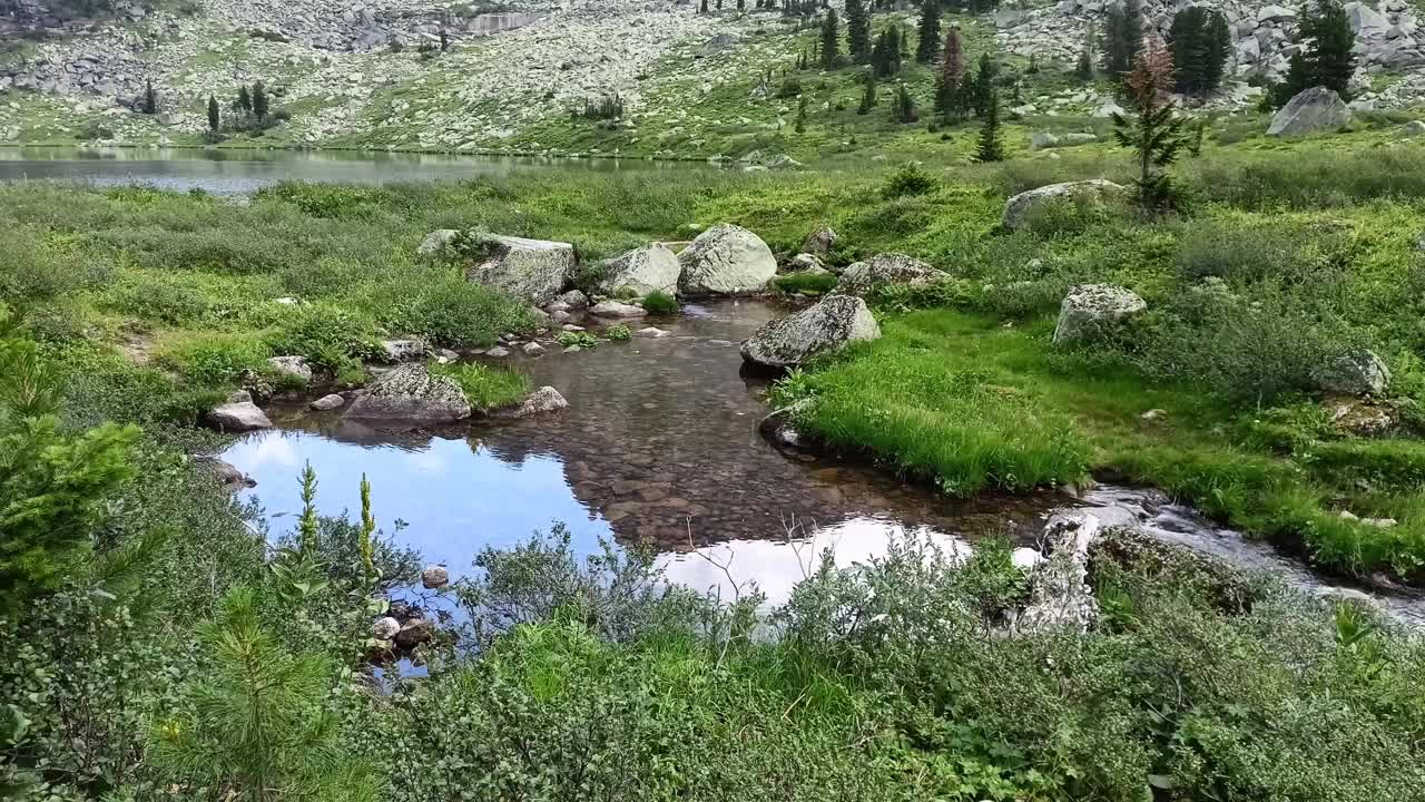 在一个平静的植物中反射出一块高高的岩石，从一个大湖泊中流过湍急的溪流。视频下载