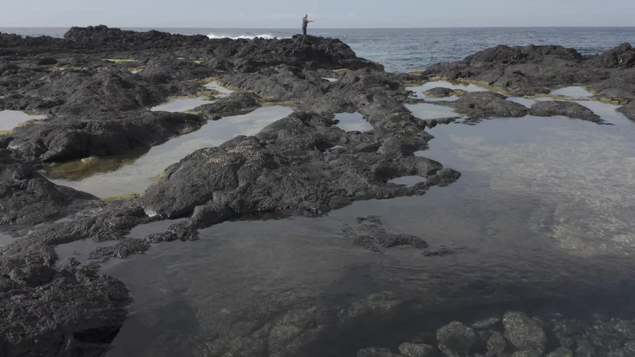 一个人在圣米格尔的莫斯泰罗斯的火山岩上探索潮汐池，用D-log自然光线拍摄视频素材