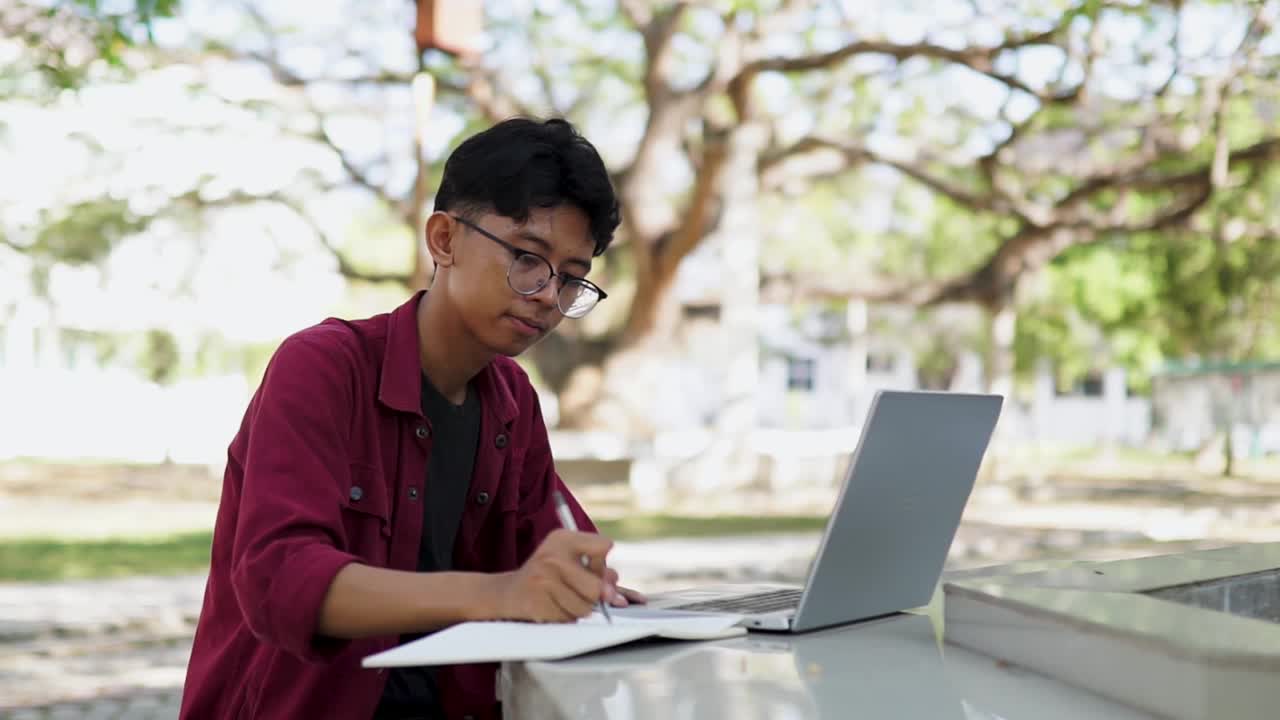 亚洲大学生在校园户外公园用笔记本电脑学习。视频下载