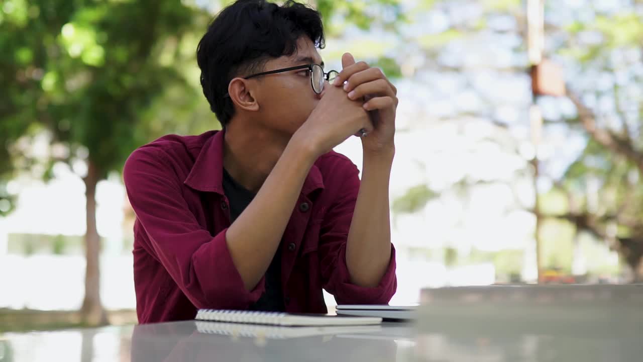 疲惫的亚洲青年大学生在学习了很长一段时间后坐在校园附近。大学生感到无聊，独自坐着视频下载