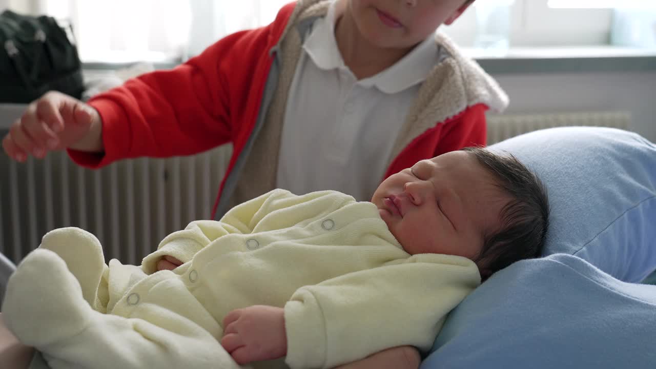 哥哥用温柔的吻拥抱新生婴儿，在舒适的室内环境中捕捉珍贵的家庭纽带和温暖视频素材