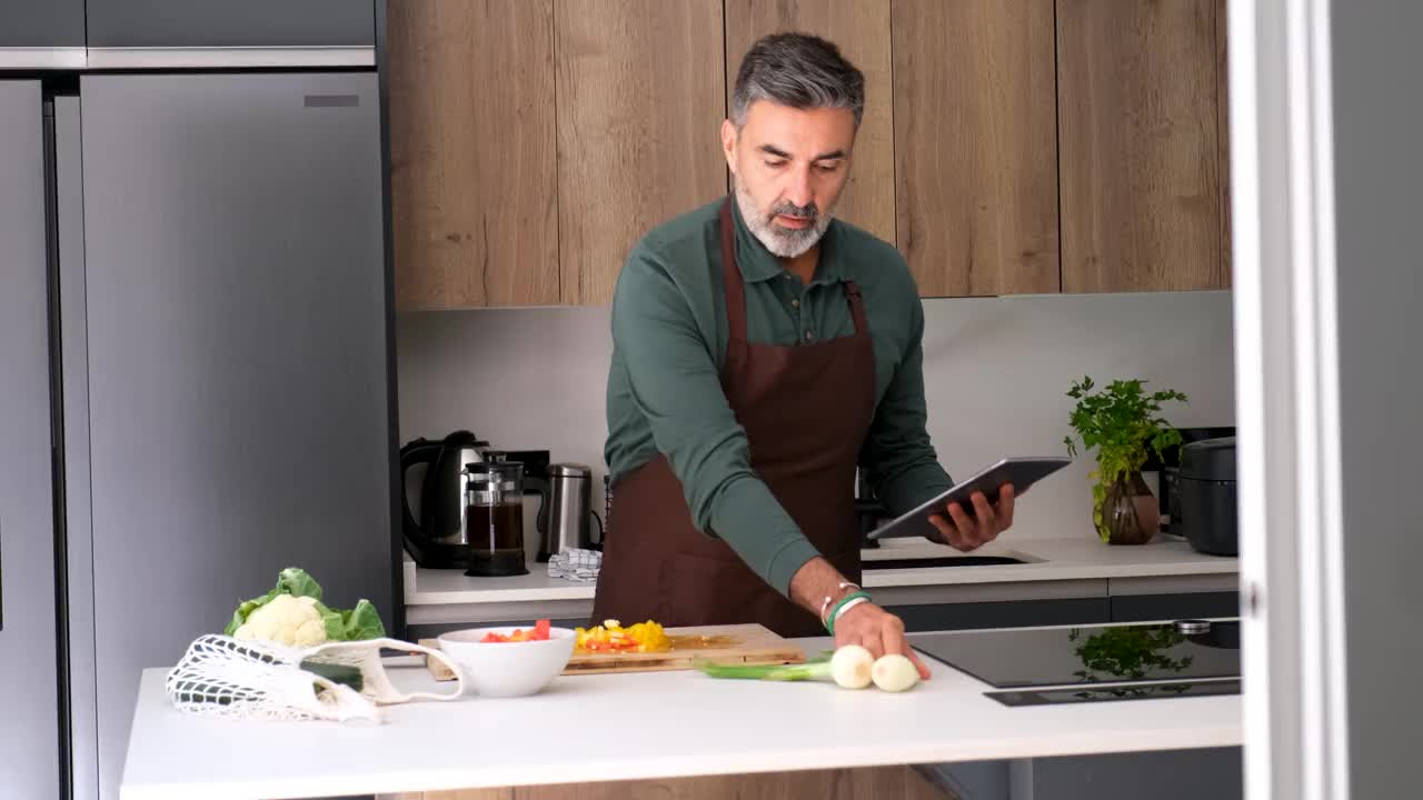 一个成熟的男人按照他的平板上的食谱，准备食物的原料视频素材