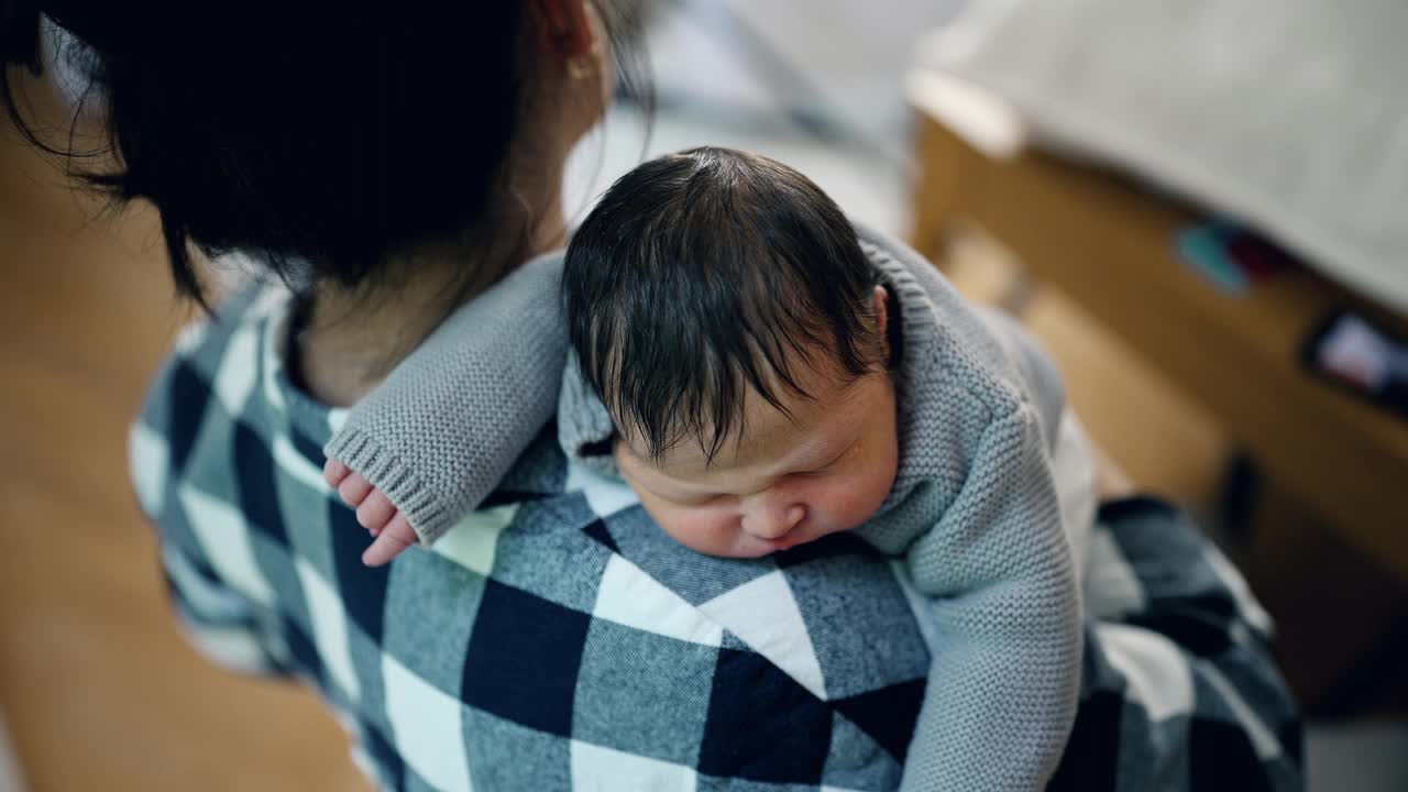 在一间宁静、阳光明媚的房间里，母亲轻轻地把她刚出生的婴儿抱在肩上。宝宝安静地睡着了，突显了他们之间的爱和温柔视频素材