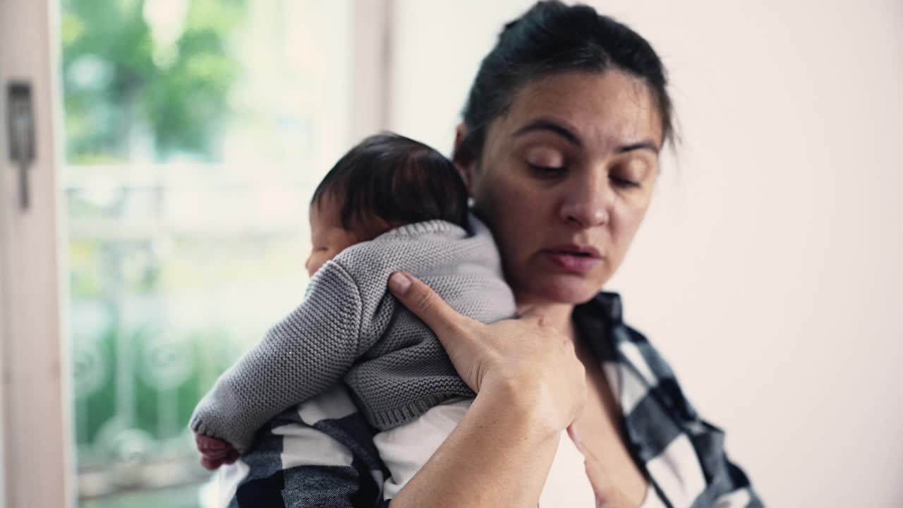 在阳光充足的房间里，一位母亲在母乳喂养后将刚出生的婴儿抱在肩上，捕捉到亲密和关怀的安静时刻。婴儿安静地躺在母亲身上视频素材