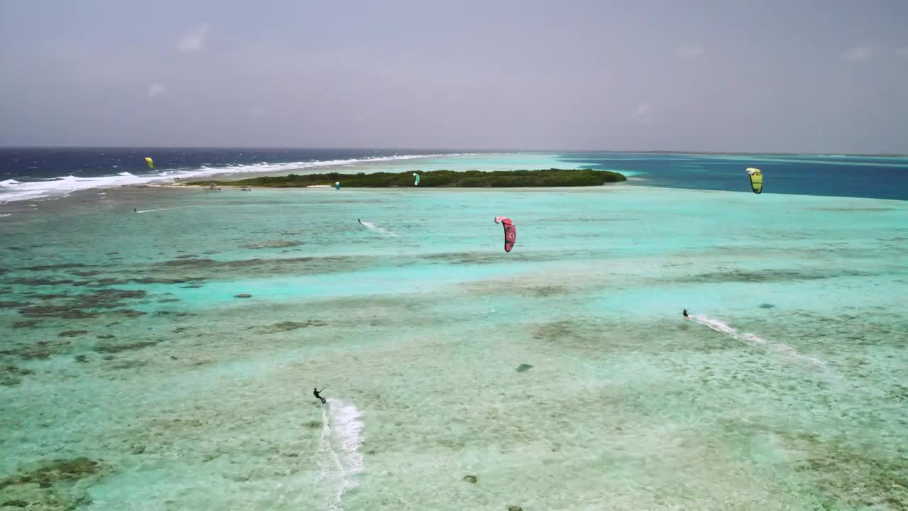 风筝冲浪者在清澈的蓝色海水中滑翔在充满活力的热带珊瑚礁上，鸟瞰图视频素材