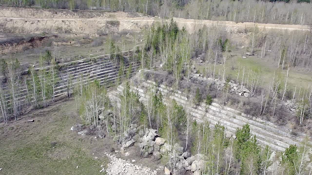 在一个阳光明媚的春日，一片巨大的空地被混交林包围，空地中央有一个废弃的大理石采石场。视频下载