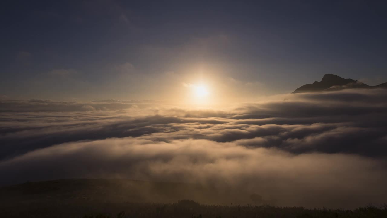 太阳从山峰之间的云层中升起的时间流逝视频素材