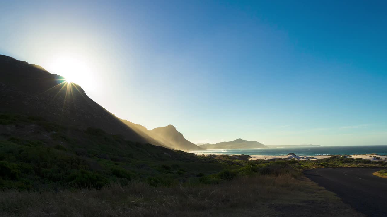 太阳在风景优美的海湾旁边的山丘上升起的时间流逝，前景是草地视频下载