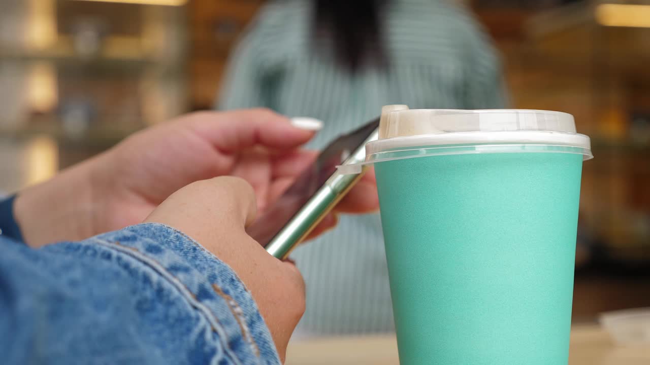 一个女人坐在咖啡店里，手里拿着手机的特写。视频下载
