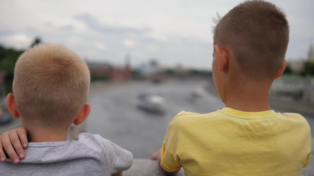 两个好奇的男孩站在城市河上的一座桥上。视频下载