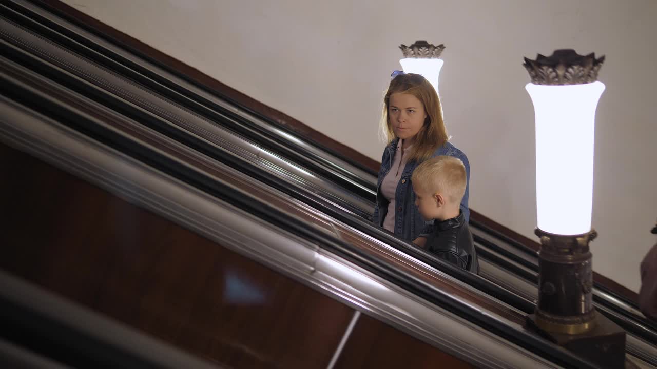 母子俩乘地铁的自动扶梯上楼。视频下载