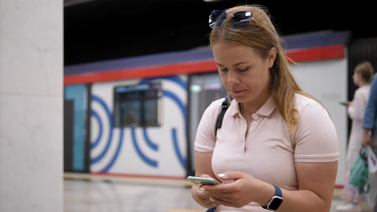 一个拿着手机的女人坐在地铁的长椅上等车视频下载