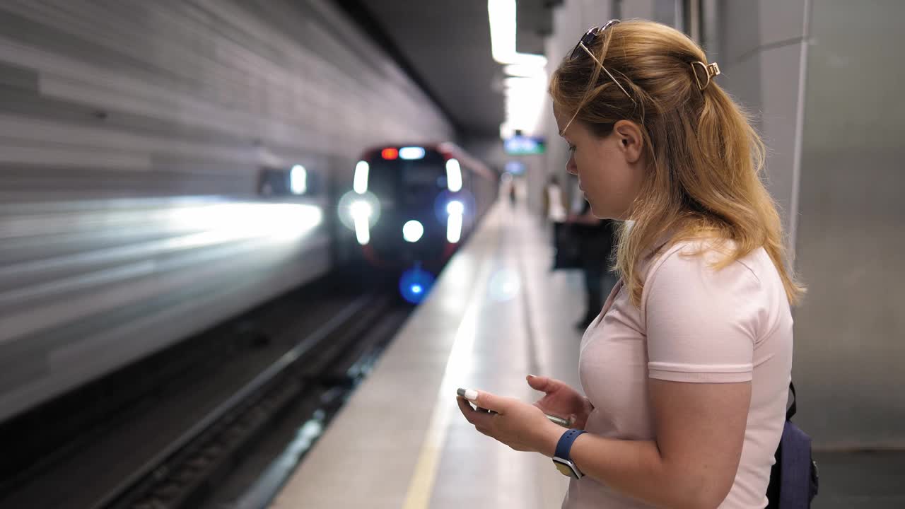 一个女人在地铁站拿着手机，背景是一列火车正在驶近视频下载