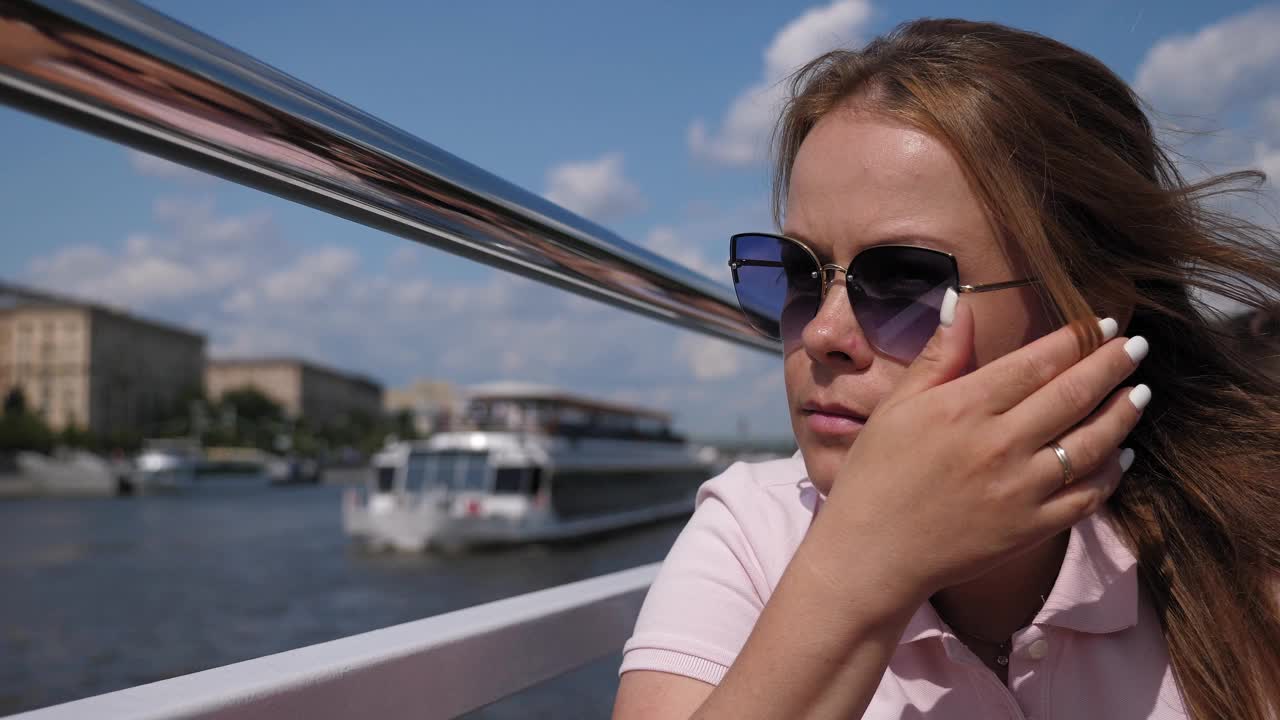一个戴着墨镜的年轻女子的特写，在刮风的天气里乘船航行。视频下载