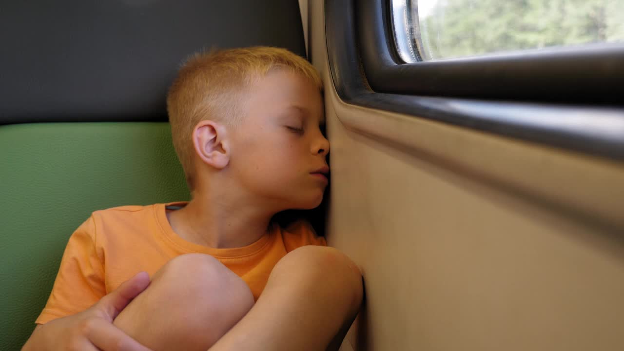 一个无聊的孩子坐在火车上，一个男孩坐在靠窗的椅子上。视频下载