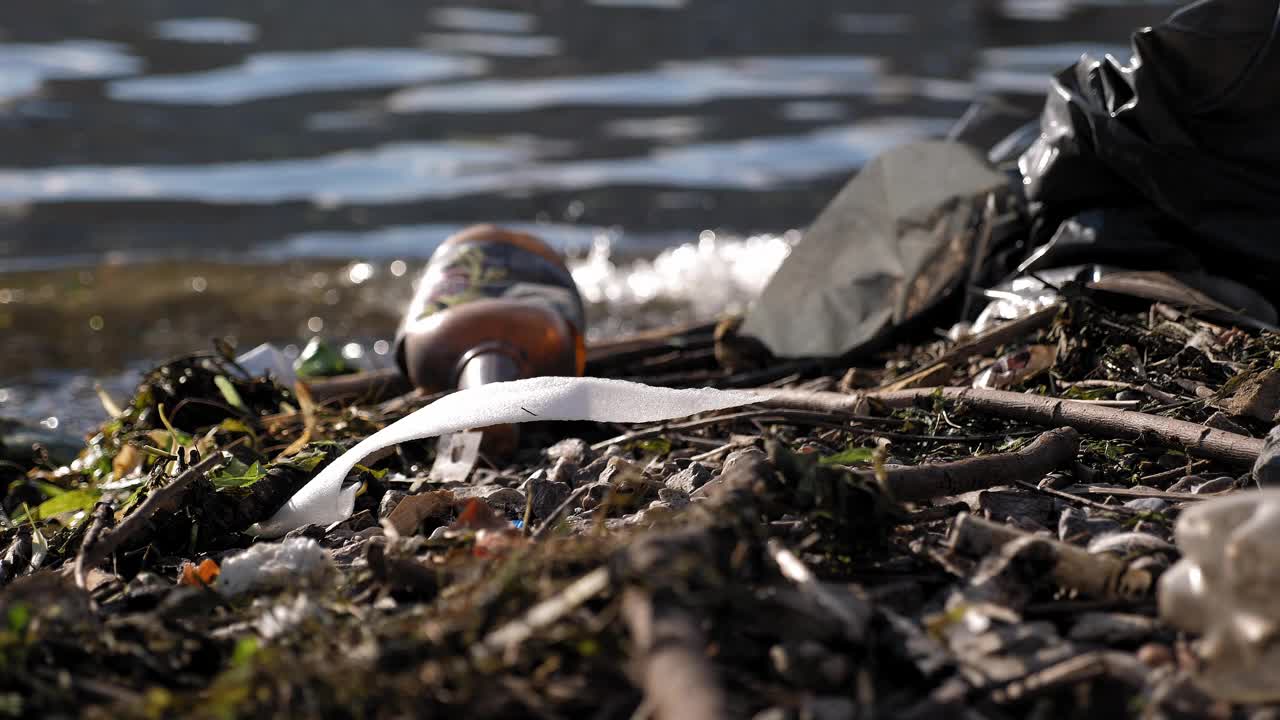 河岸上的塑料垃圾、瓶子和袋子的特写。视频下载