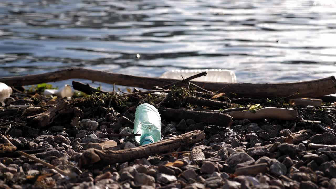 河岸上的塑料垃圾、瓶子和袋子的特写。视频下载