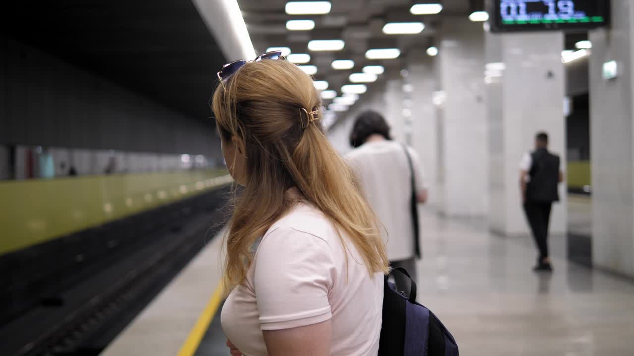 一位妇女站在灯火通明的地铁站台上等火车。视频下载