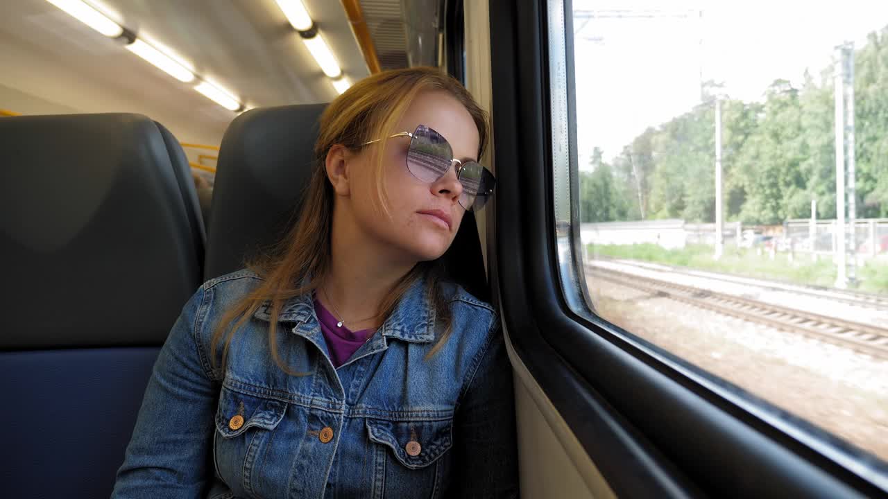 火车上，一位戴着墨镜的疲惫的妇女斜着身子望着窗外。视频下载