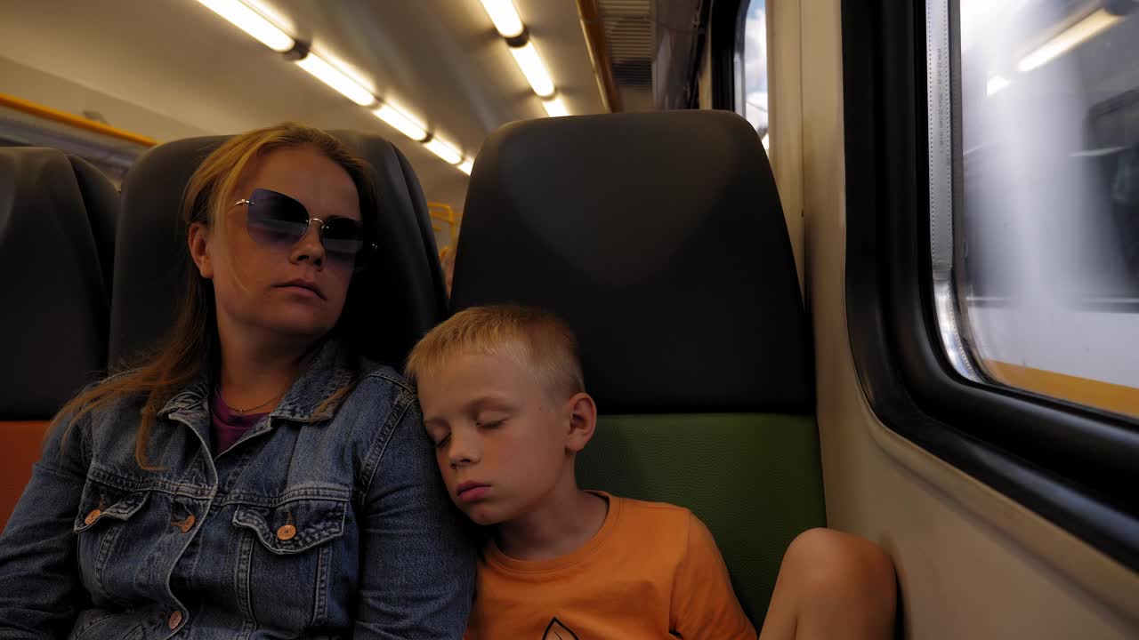 母子俩在火车上睡觉，小男孩靠在妈妈身上。视频下载