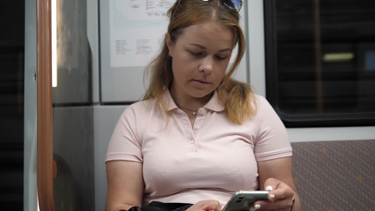一位年轻女子坐在地铁车厢里使用她的智能手机。视频下载