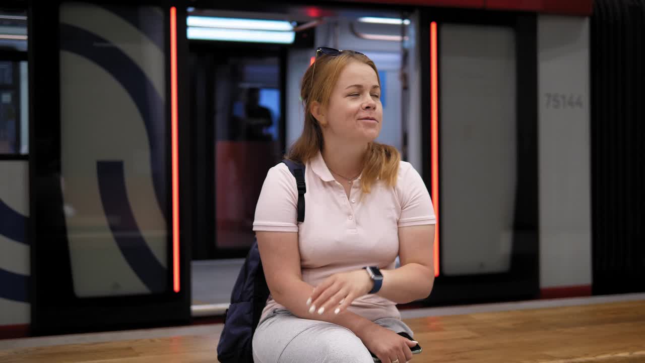一个背着背包的年轻女子坐在地铁站的长椅上。视频下载