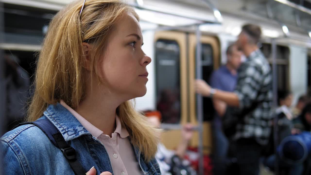 一个穿着牛仔夹克的女人站在地铁车厢里，抓着扶手。视频下载
