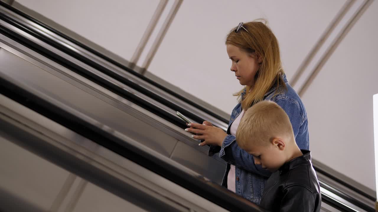 母子俩手里拿着手机爬地铁的自动扶梯。视频下载