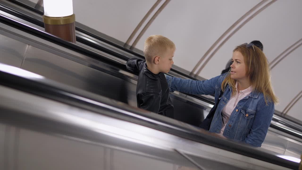 一对快乐的母子爬上地铁的自动扶梯，愉快地交谈着。视频下载