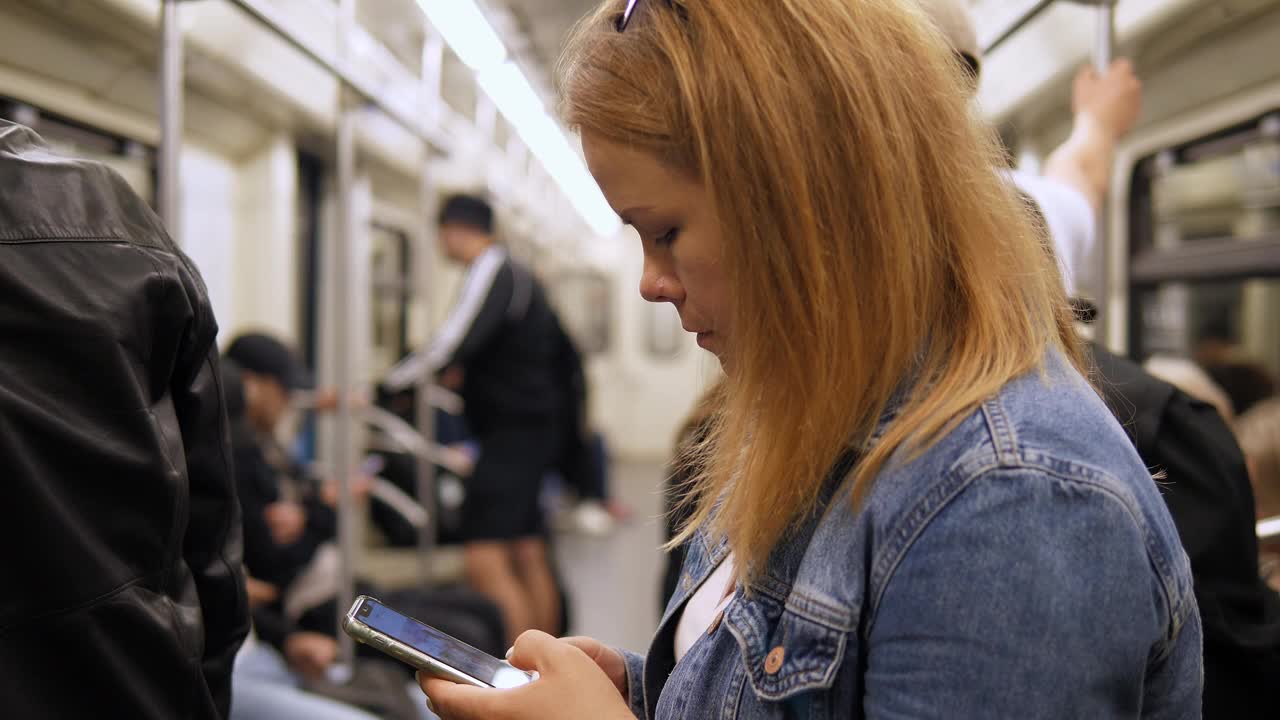 一个年轻女子在拥挤的地铁车厢里拿着手机的特写镜头。视频下载