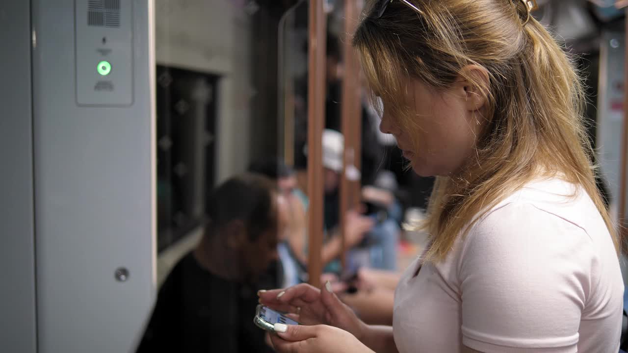 一名年轻女子在满车的地铁车厢里手里拿着手机。视频下载