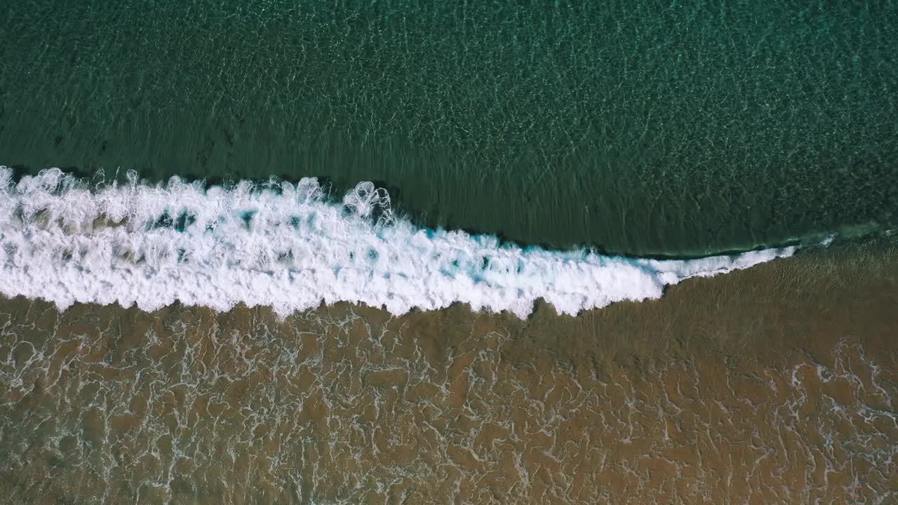 鸟瞰图，一个波浪沿着海岸在清澈的浅水中破碎视频素材