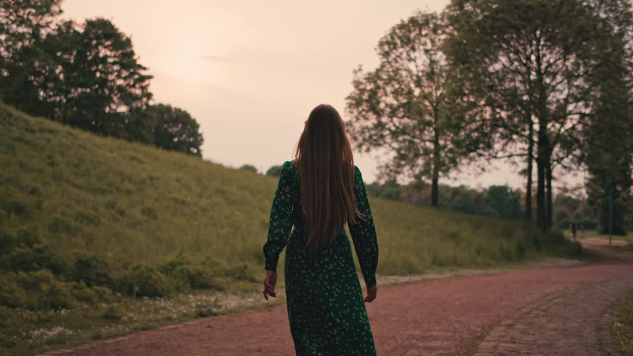 年轻美丽的女人在夏日的大自然中穿着绿色的长裙散步。视频素材