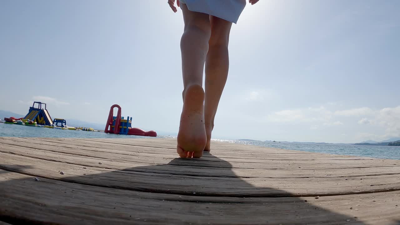 一个优雅的女人的脚走在码头上的绿松石海水在热带岛屿，慢动作视频素材