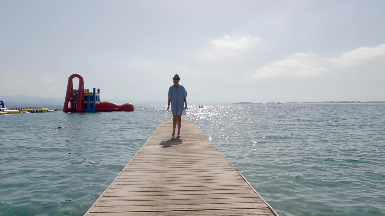 一个迷人的女人走在一个热带岛屿的木制码头上，从前面到后面，慢动作的电影转换视频素材