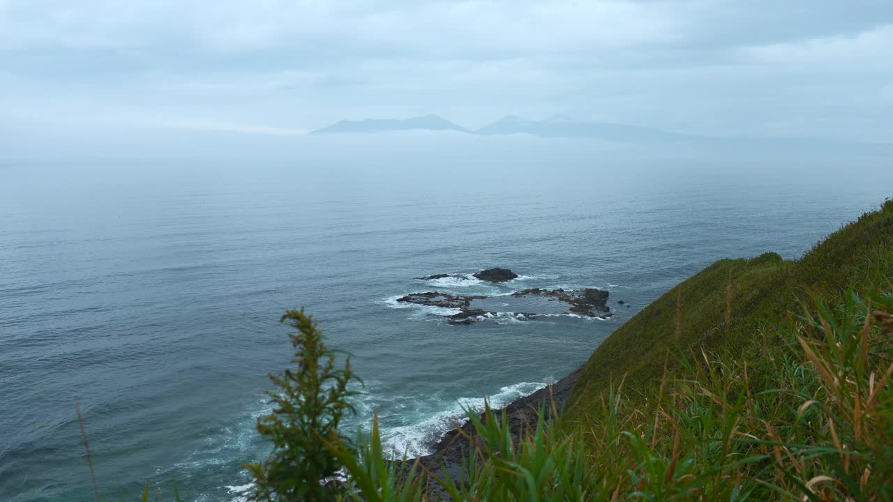 从绿色的山顶到阴天的海洋地平线的美丽景观。夹。美丽的绿草在海边的山脊上。绿草如茵的山岸和阴天的海地平线。视频素材