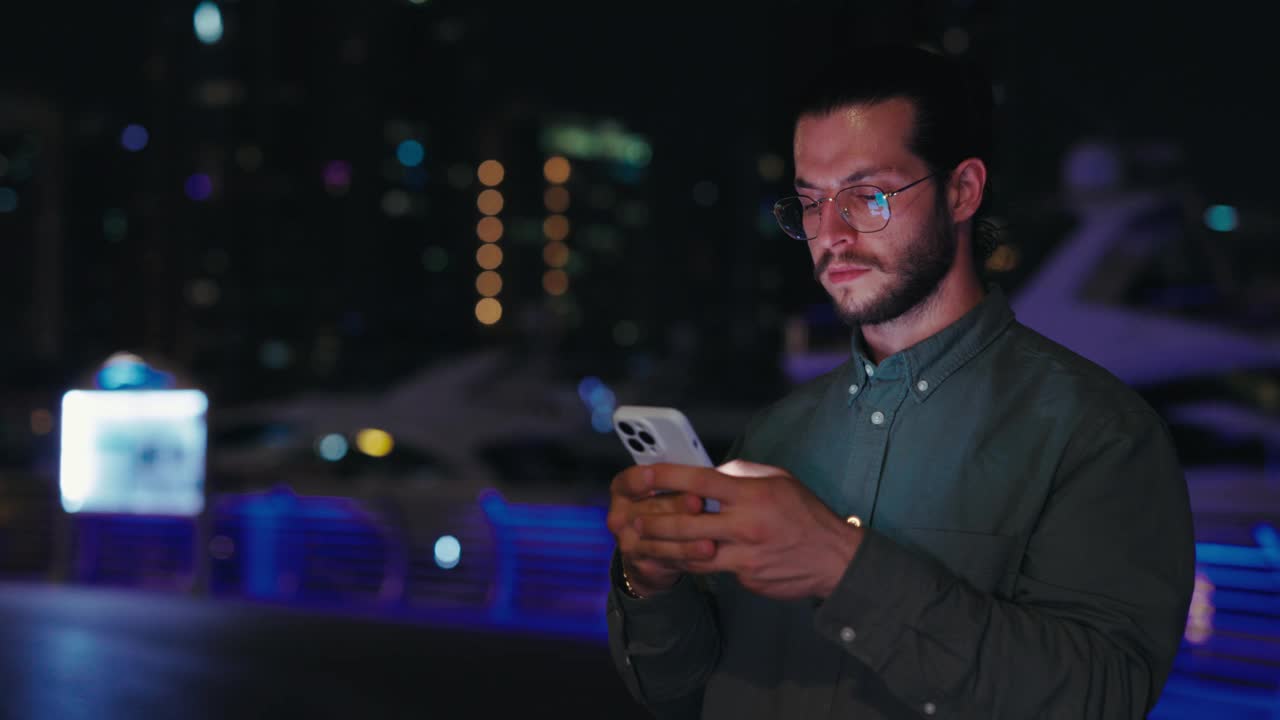 戴眼镜的严肃男人站在夜城，在社交网络上聊天。视频素材