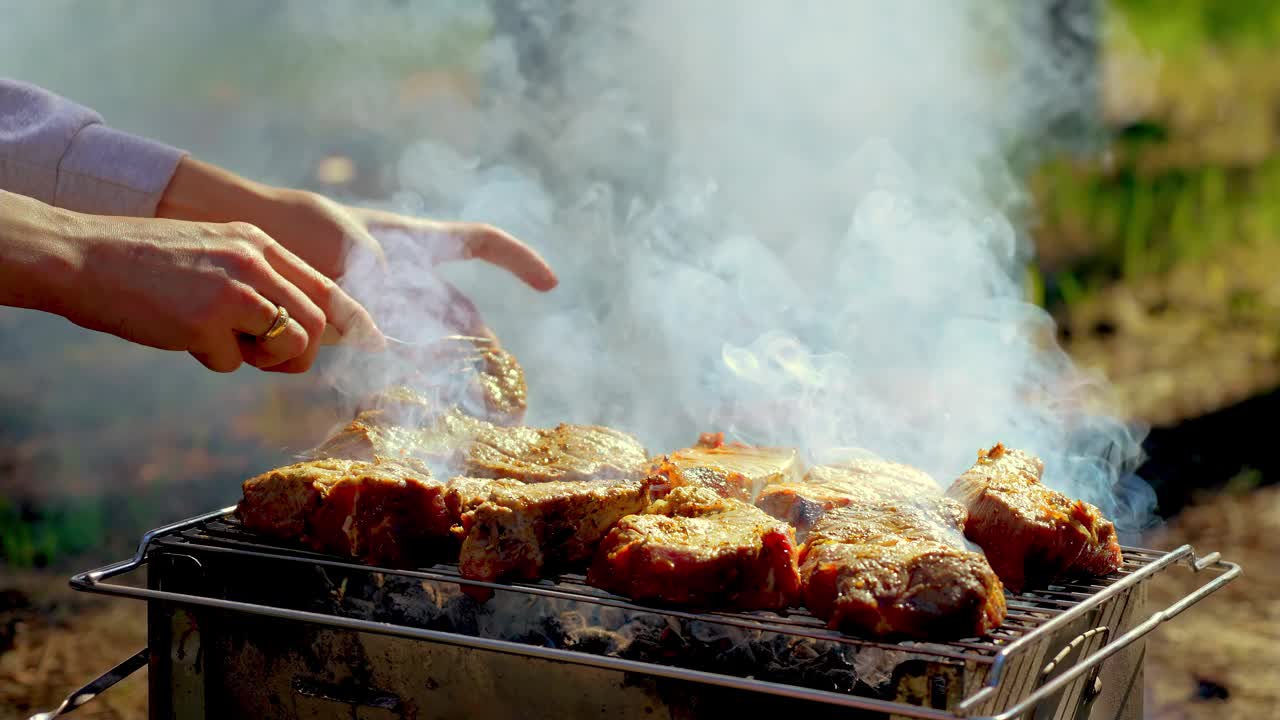 面目全非的女人正在翻动用香料腌制的烟熏多汁的肉块，这些肉块在炭火上烤着视频素材