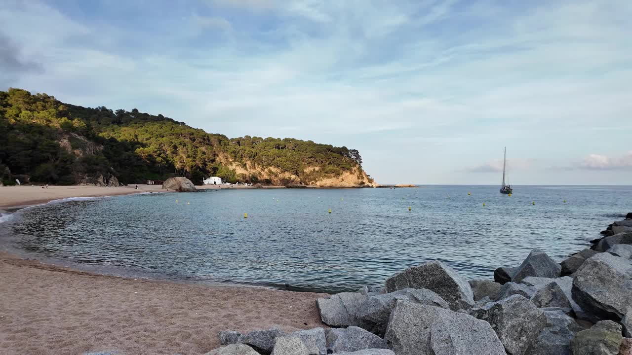 美丽的海景，日落时西班牙空旷的海滩，背景是地平线上的一艘帆船视频下载