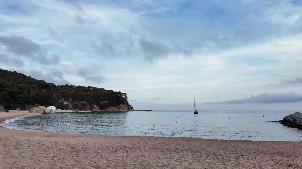 美丽的海景，日落时西班牙空旷的海滩，背景是地平线上的一艘帆船视频下载