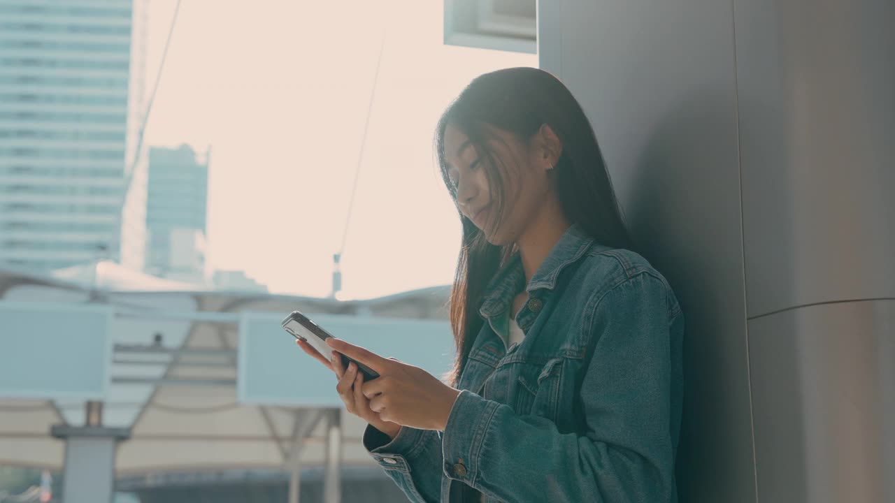 年轻的亚洲女子站在城市里，在街上使用手机视频素材