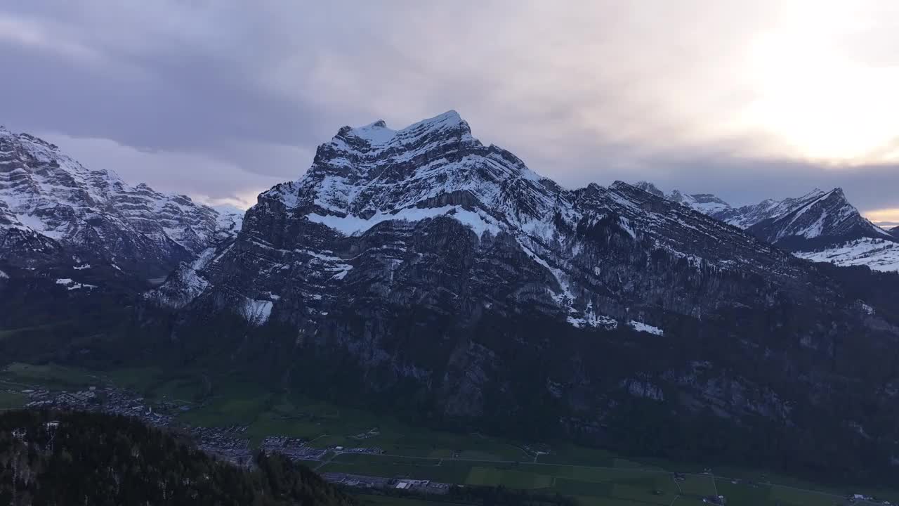 日落时瑞士阿尔卑斯山白雪皑皑的壮丽景色。引人注目的山峰部分被雪覆盖，下面是一个宁静的山谷，在多云的天空下。视频素材