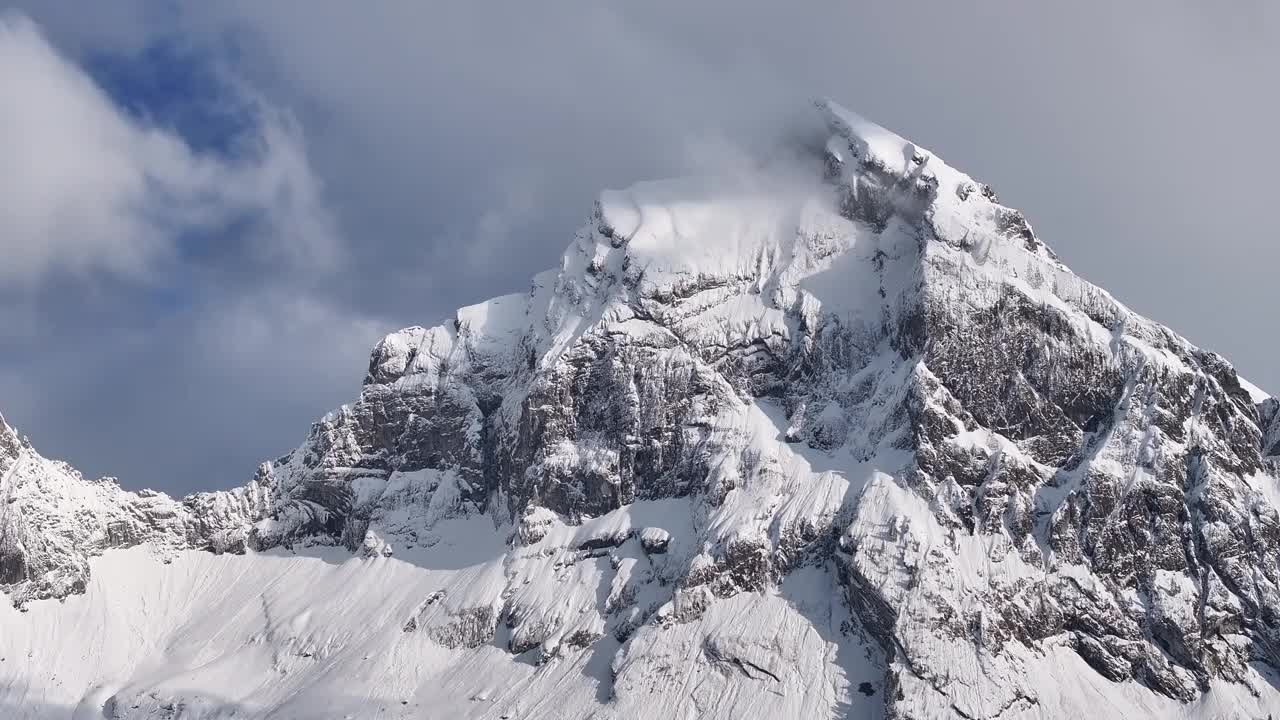 瑞士阿尔卑斯山脉一座雄伟、白雪覆盖的山峰的特写。在部分多云的天空下，崎岖的岩层和新鲜的雪创造了令人惊叹和戏剧性的景观。视频素材