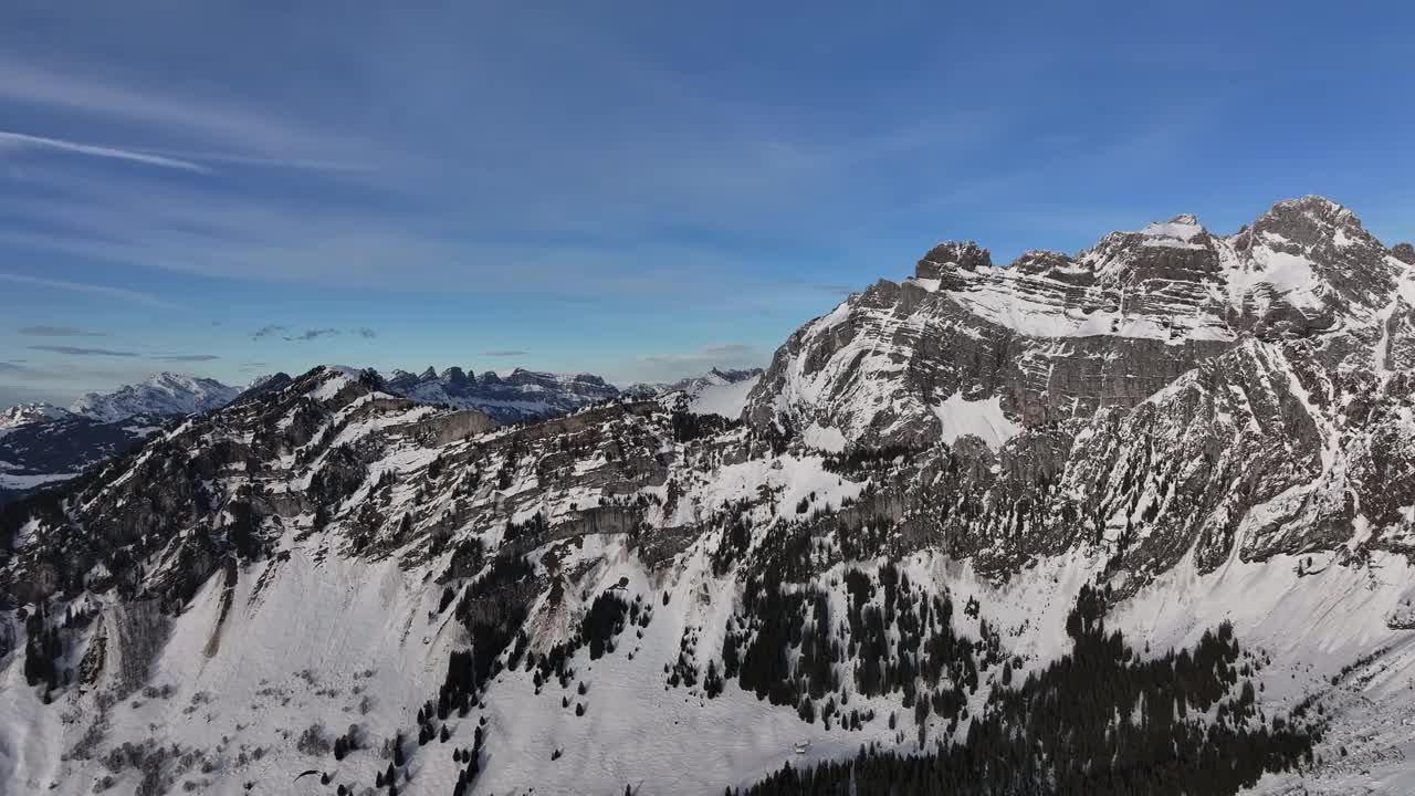 晴朗蓝天下瑞士阿尔卑斯山的鸟瞰图。崎岖的山峰和白雪皑皑的山坡创造了令人惊叹和戏剧性的景观，非常适合冬季冒险视频素材