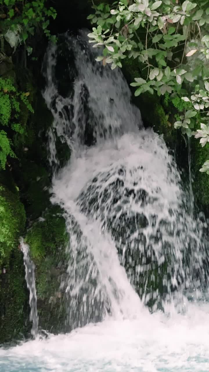 小瀑布流入一条湍急的绿松石山河。该视频突出了在自然环境中流动的水之美，展示了充满活力的绿松石河及其动态流动视频素材