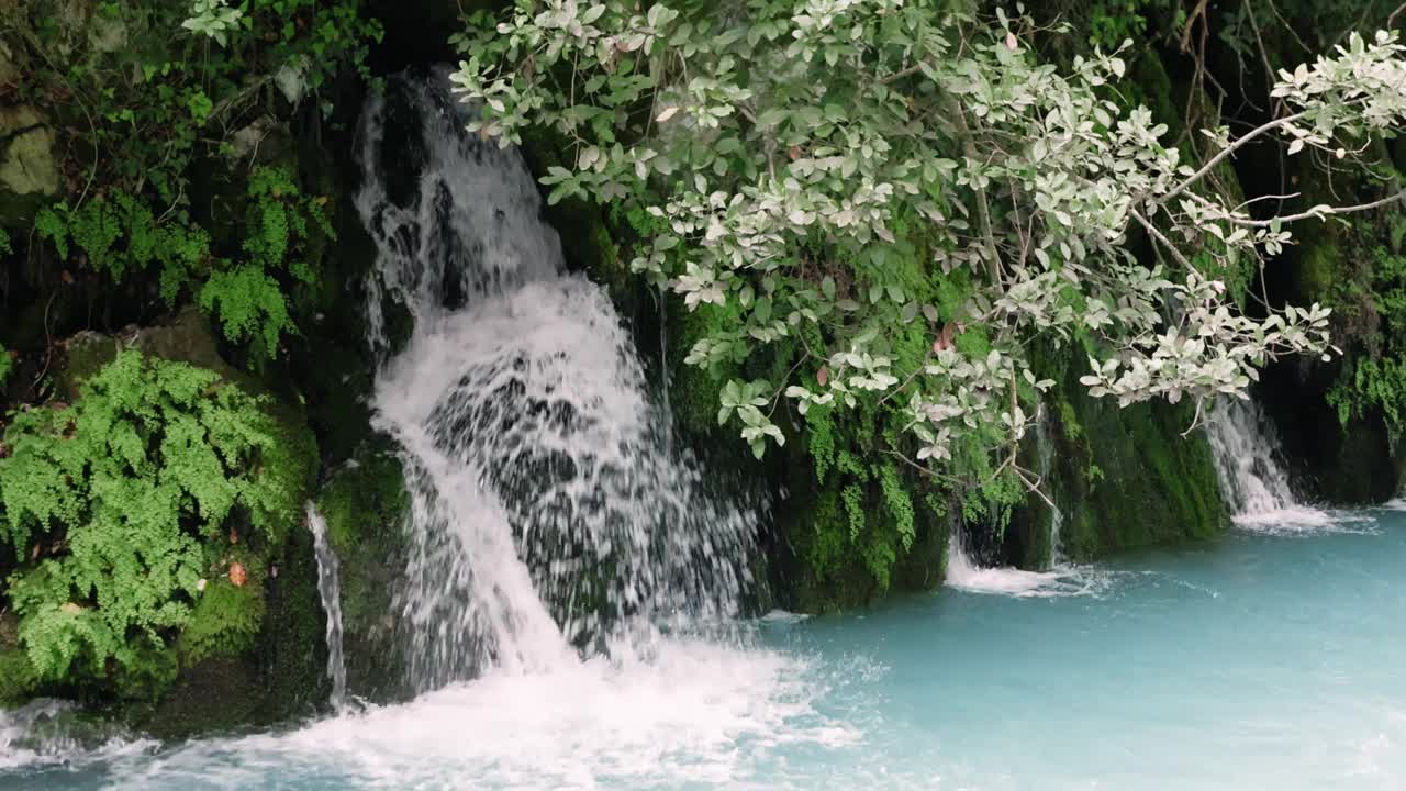 小瀑布流入一条湍急的绿松石山河。该视频突出了在自然环境中流动的水之美，展示了充满活力的绿松石河及其动态流动视频素材