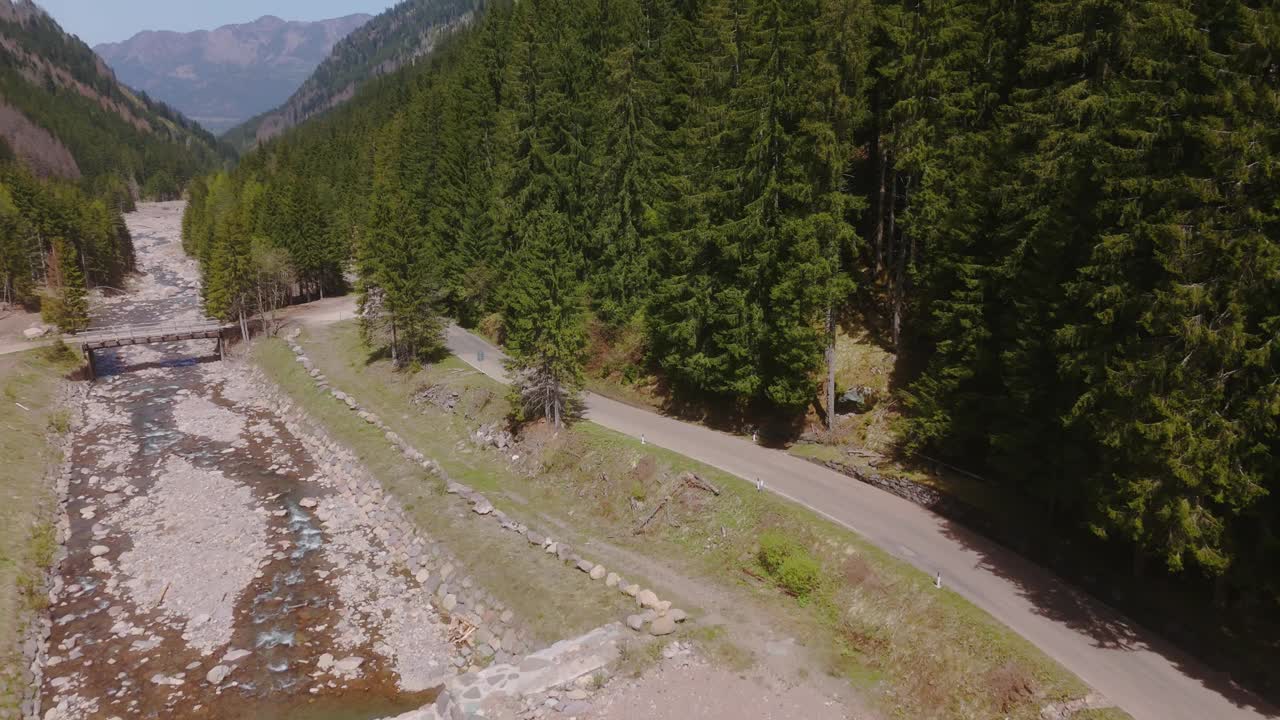 一条蜿蜒的道路穿过郁郁葱葱的森林，旁边是山中的岩石河流视频素材