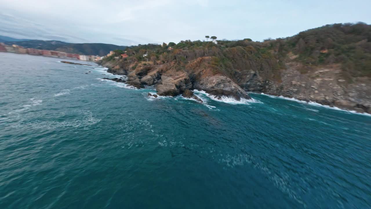 FPV无人机飞过岩石海岸线，蓝色的海洋和遥远的城镇视频素材