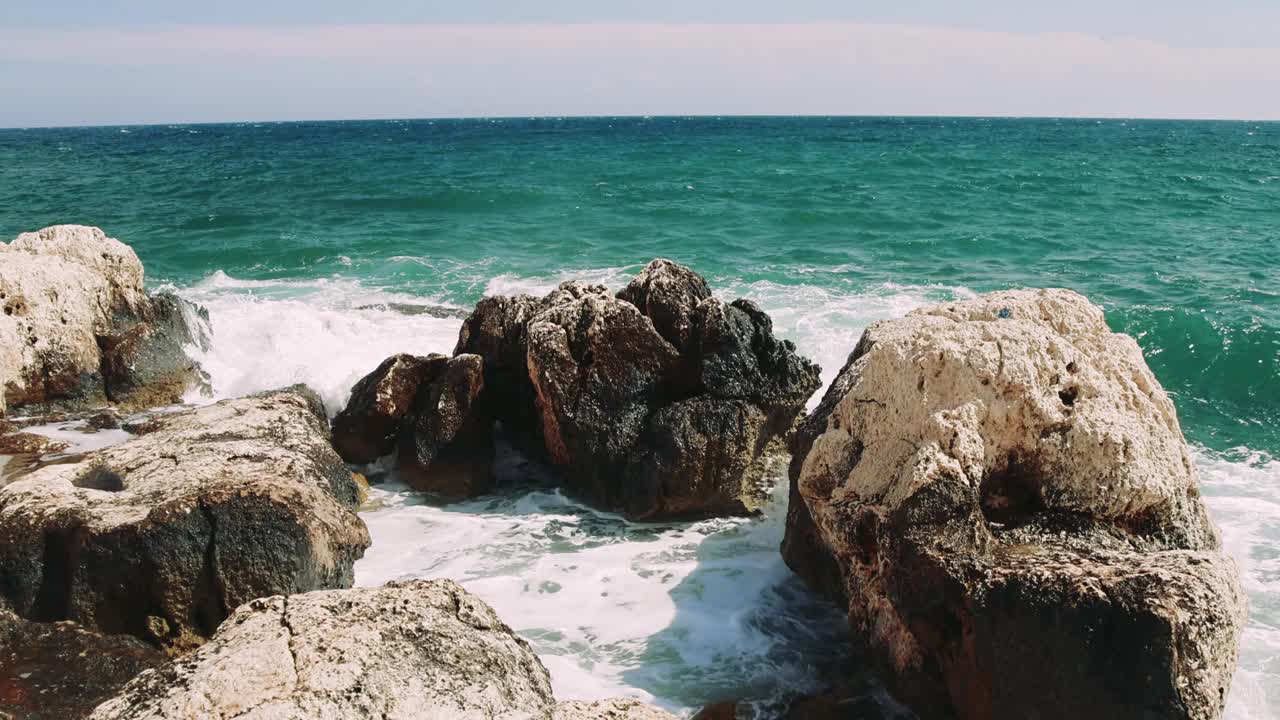 宁静的舞蹈:岩石在绿松石波浪上的平衡观看一组岩石在闪闪发光的绿松石波浪上微妙地平衡，随着海浪的每一次撞击轻轻地摇摆。视频素材